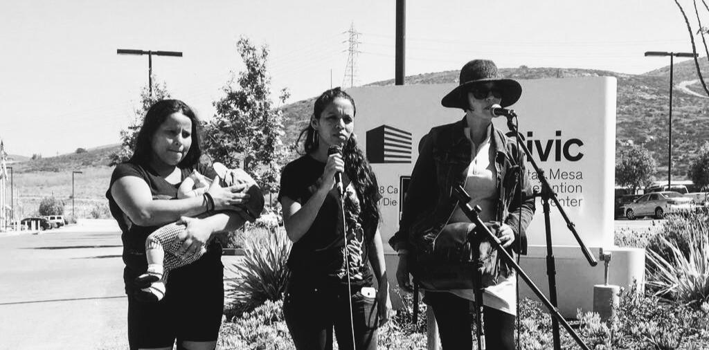 Three people and a baby stand in front of the Otay mesa Detention Center